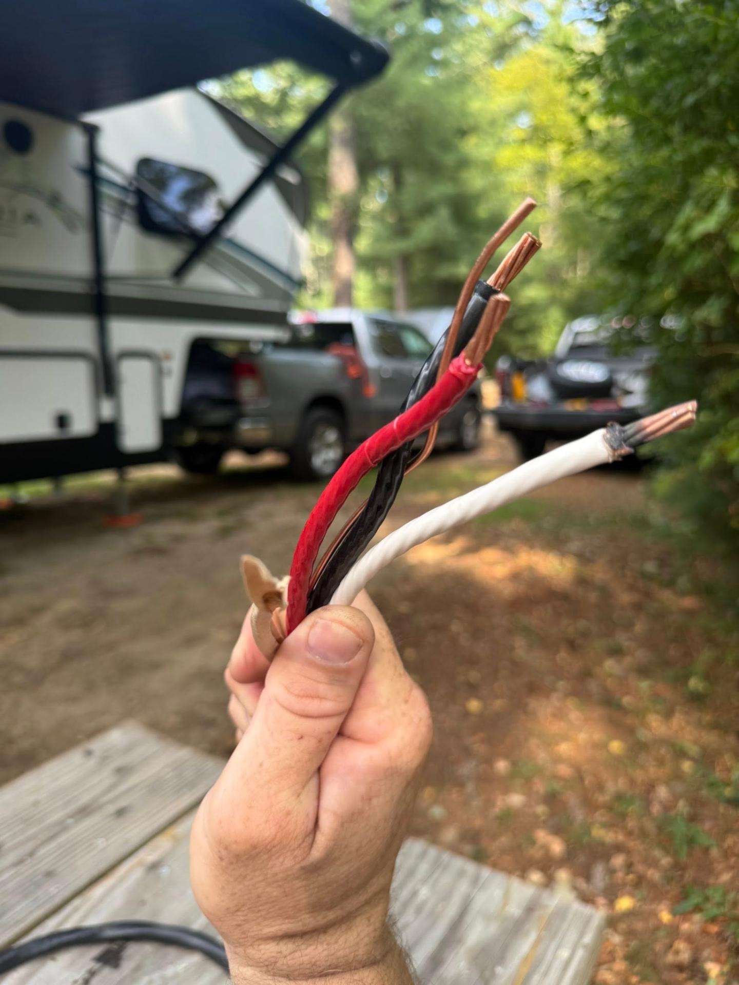 Damaged RV power cord wires held up showing exposed copper conductors and worn insulation