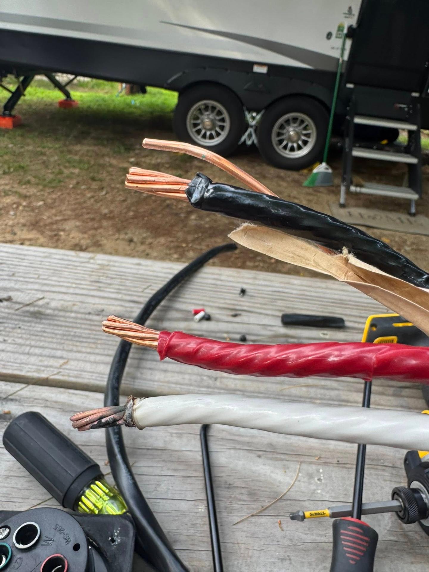 Heavy gauge RV power wires stripped and prepared for connection with an RV visible in the background
