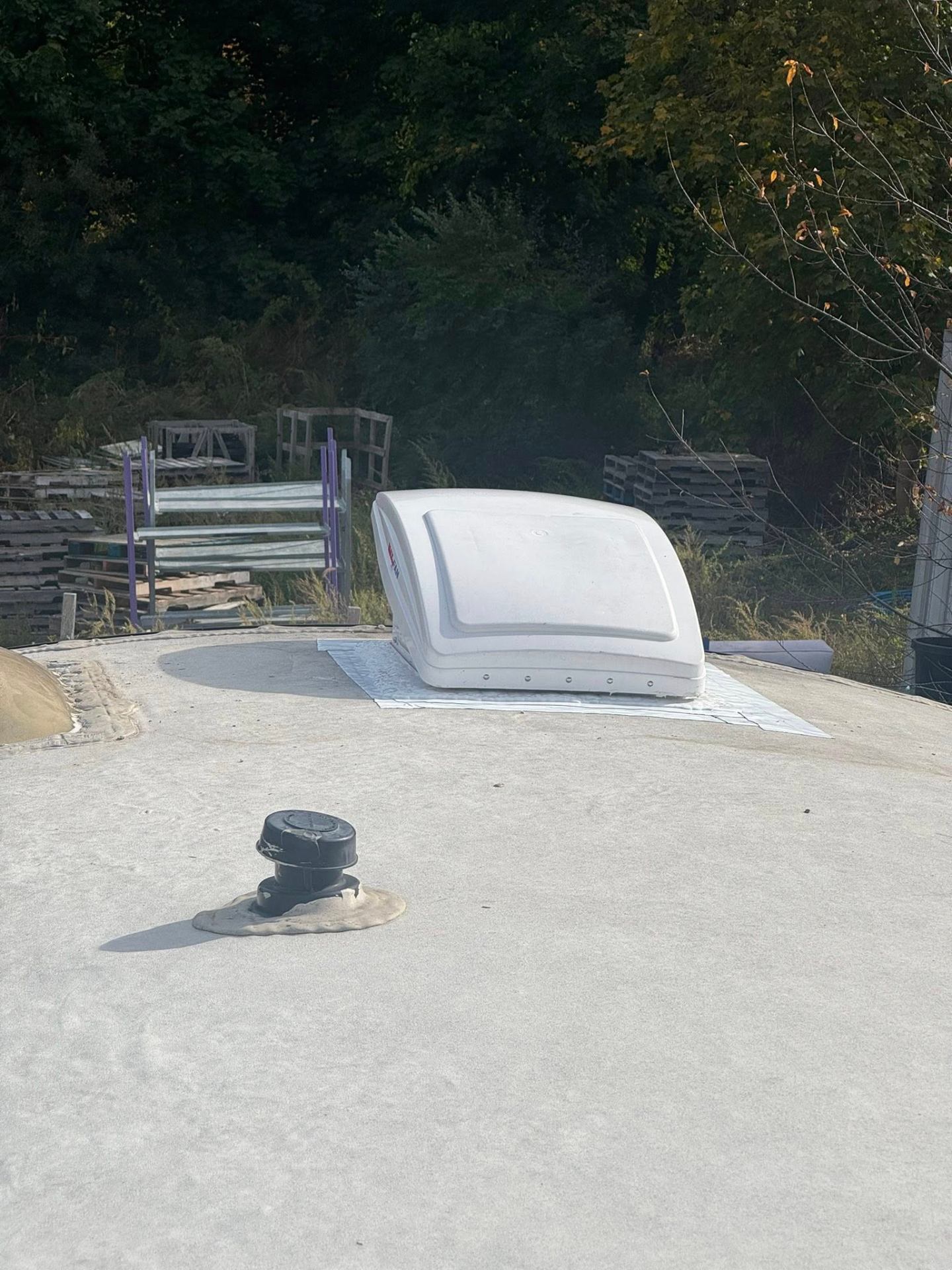 Completed RV roof vent installation with fresh sealant and plumbing vent cap on a clean roof surface