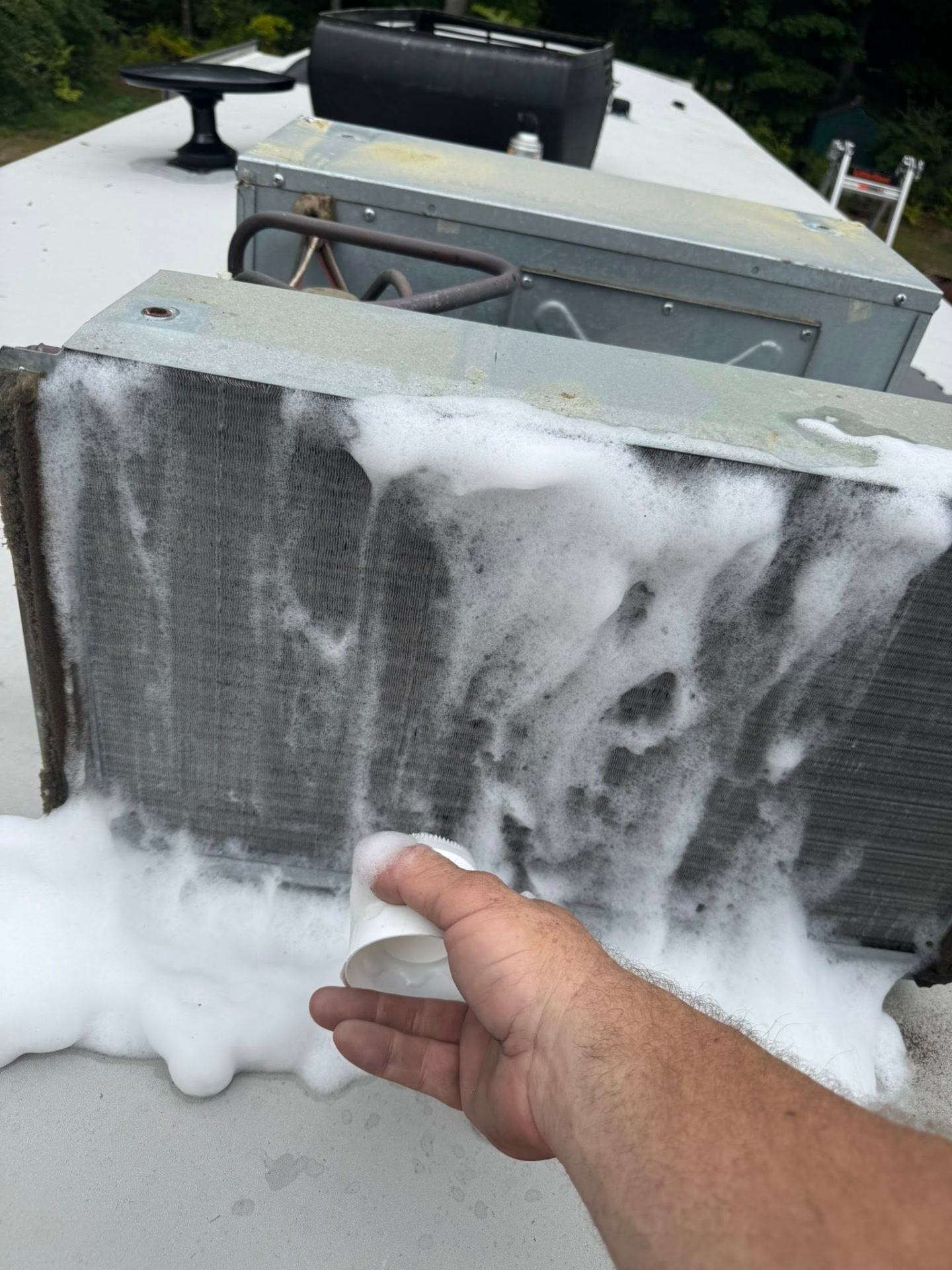 Foaming cleaner being applied to a dirty RV air conditioner condenser coil on the roof