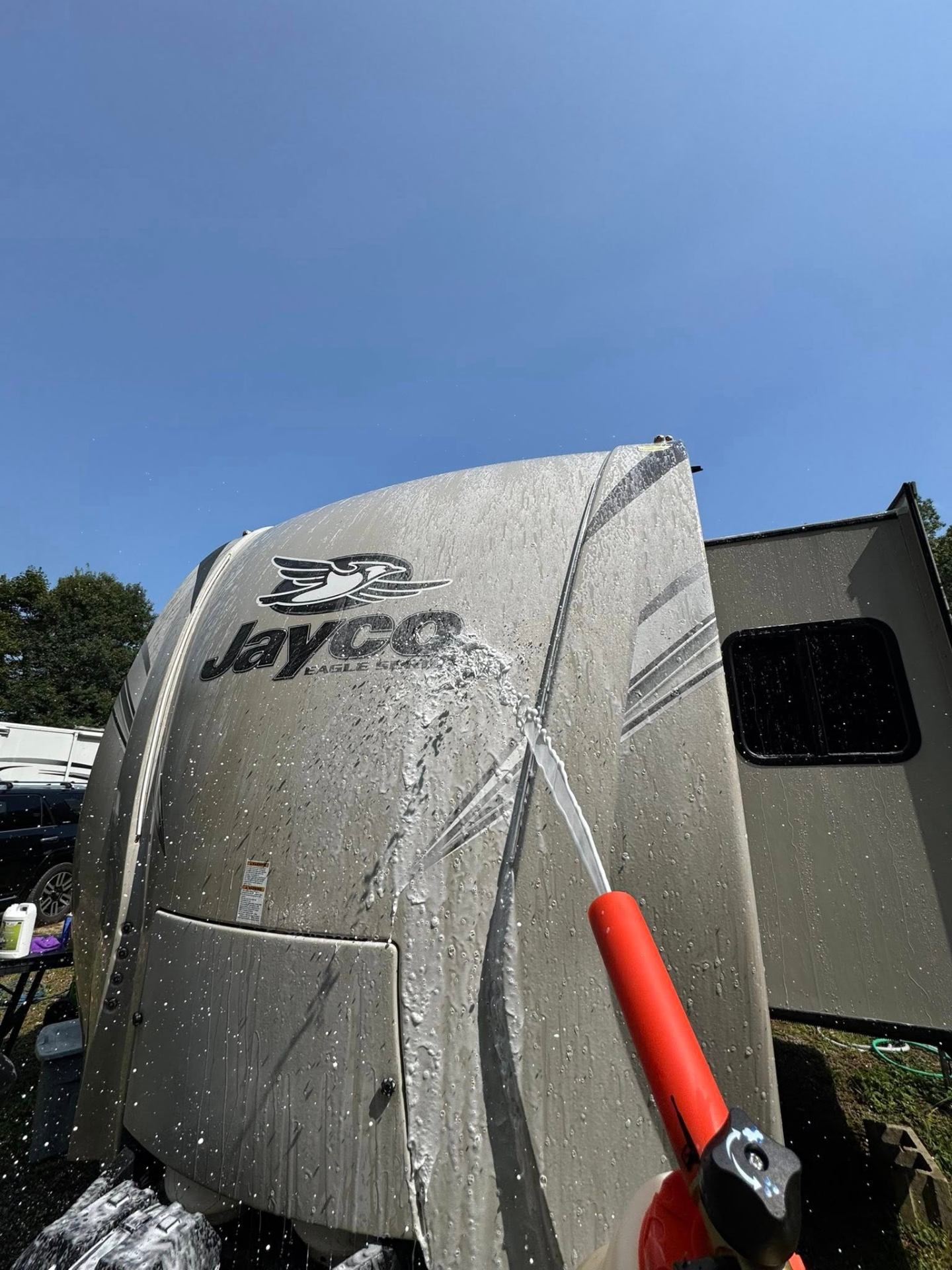 Rinsing the exterior of a Jayco Eagle travel trailer with a hose during a professional RV wash