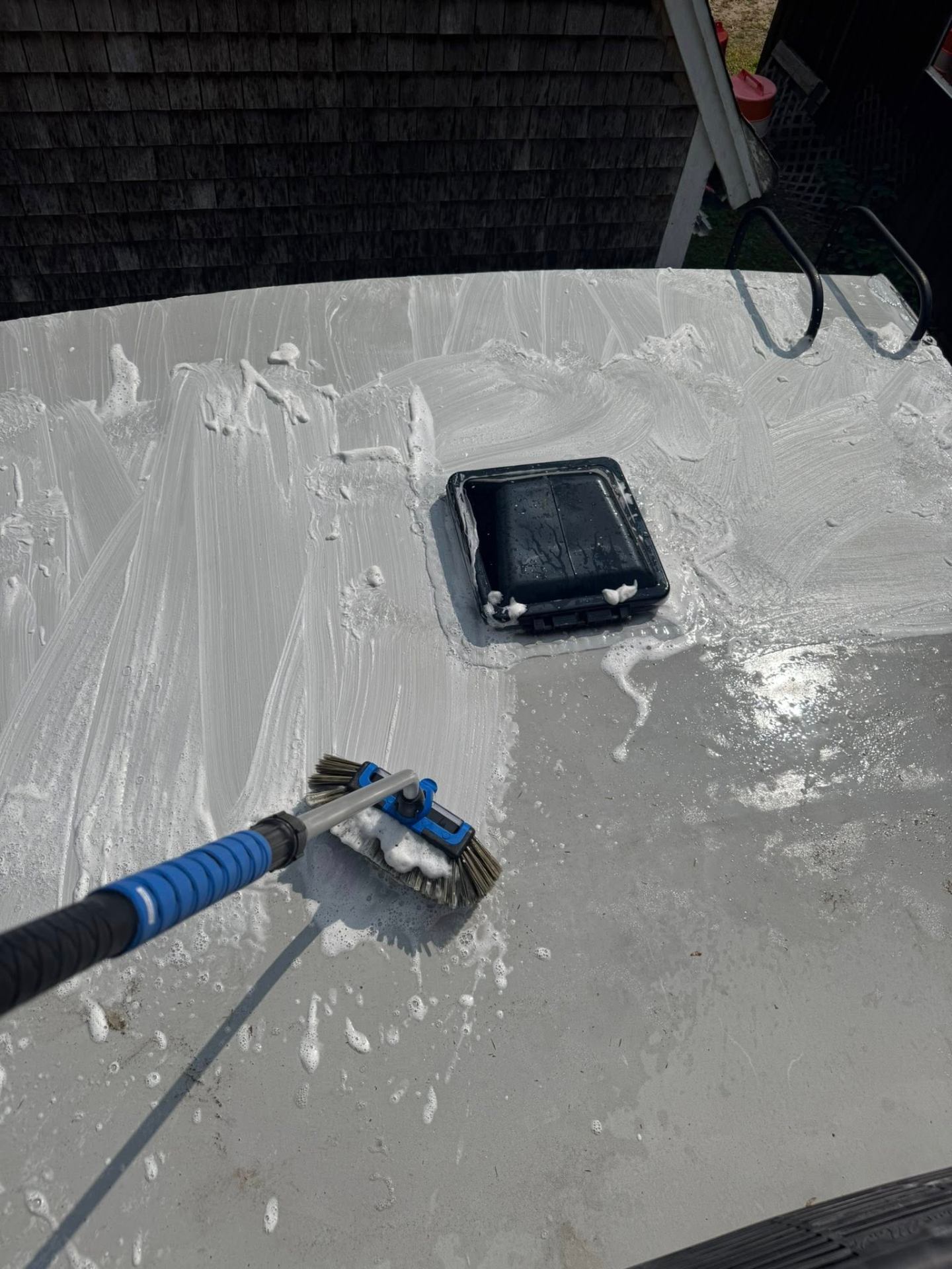Scrubbing an RV roof with a brush and soap around a roof vent during a professional wash